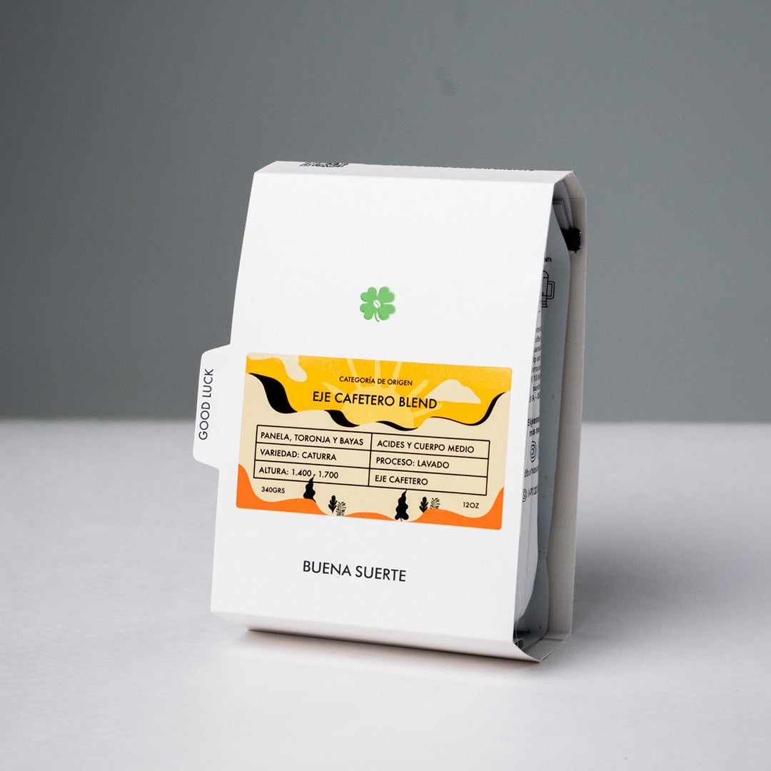 Bolsa blanca Buena Suerte con etiqueta naranja y amarilla Eje Cafetero Blend sobre fondo gris